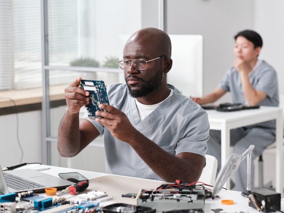 Young serious repairman looking at circuit board of electronic device in his hands