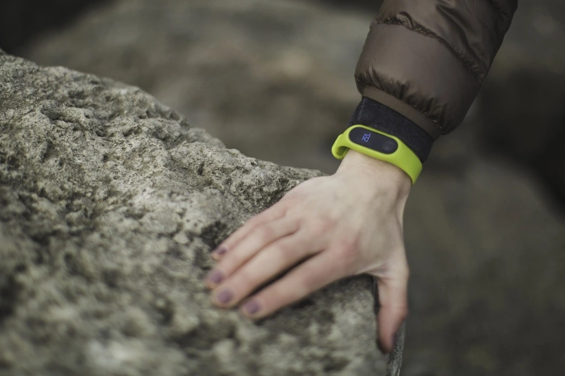 Person's arm with wearable technology device (Fitbit) holding onto a rock for support.