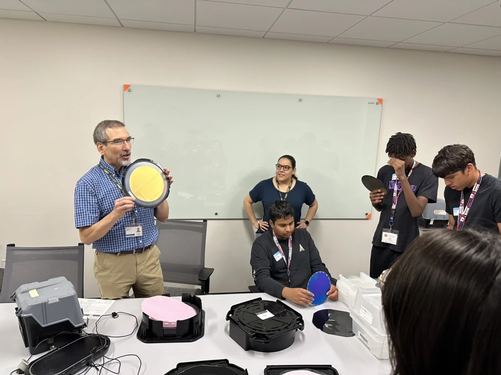 Presenter holding wafer talks to semiconductor camp students.